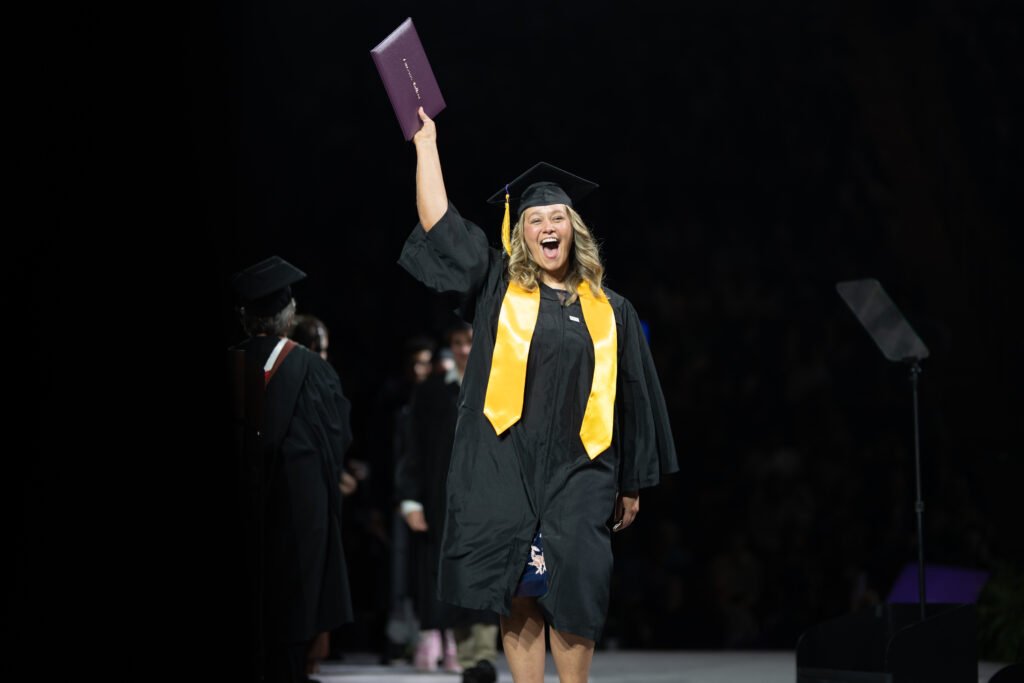 A woman holds up her diploma joyfully