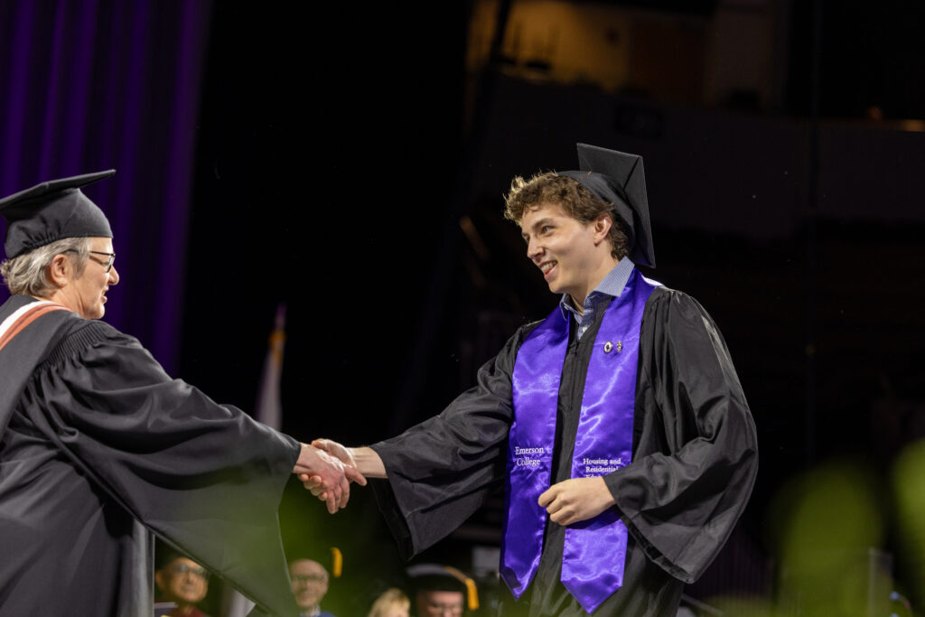 A student shakes someone's hand while receiving their diploma
