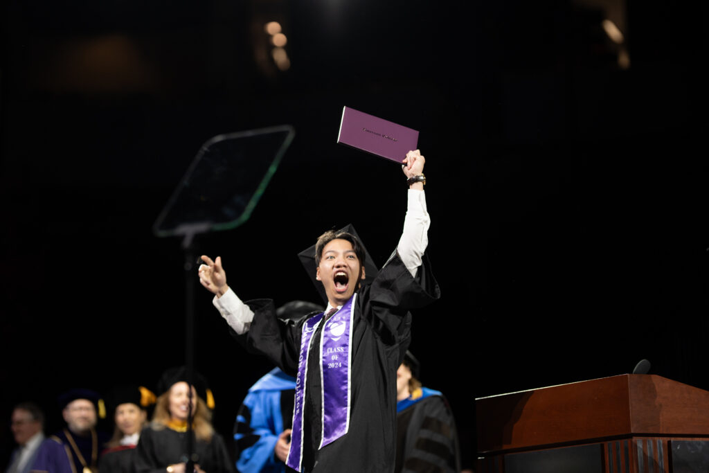 A student holds up their diploma and cheers to the crowd