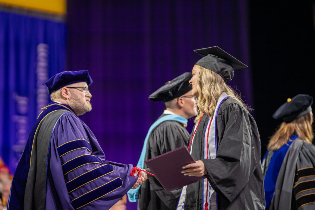 Jay Bernhardt shakes a student's hand who just received her diploma