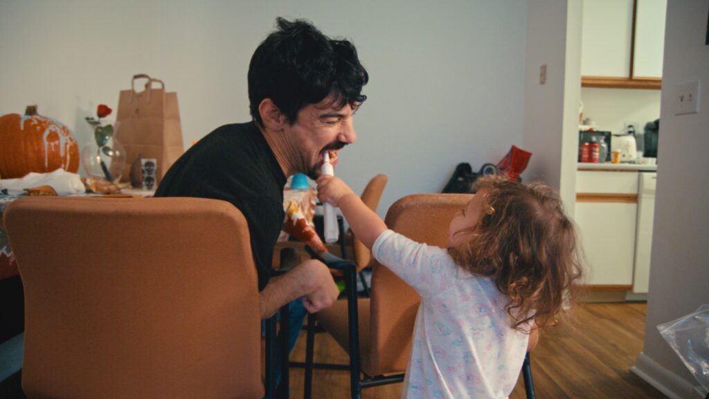 Alexander Freeman plays with his daughter while he sits in a chair, she's brushing his teeth