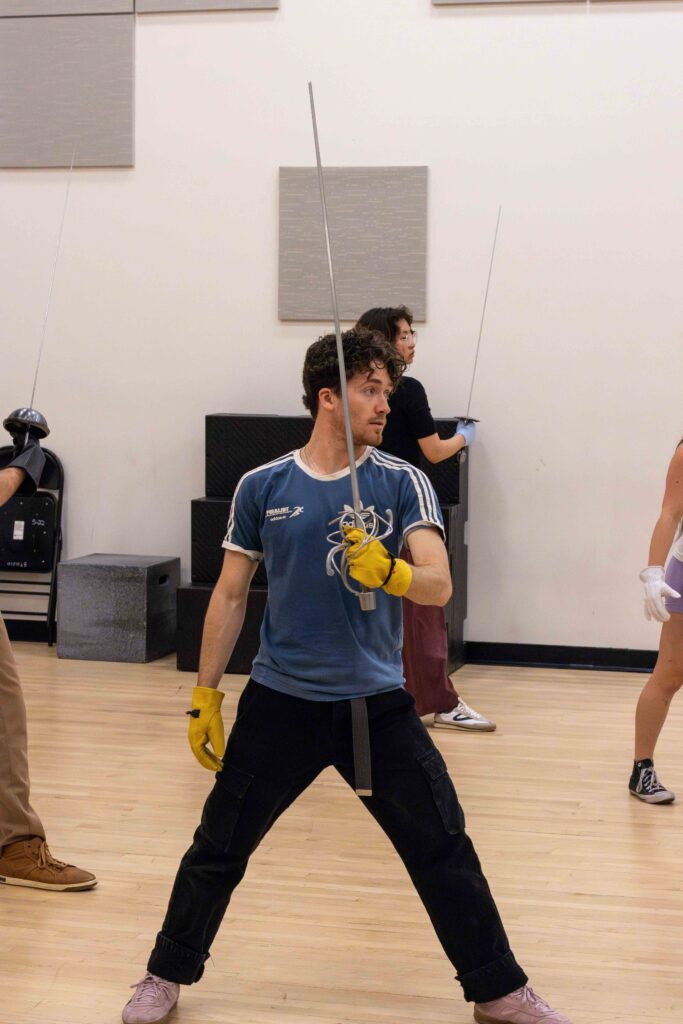 A student holds a blade up while wearing a yellow dueling glove