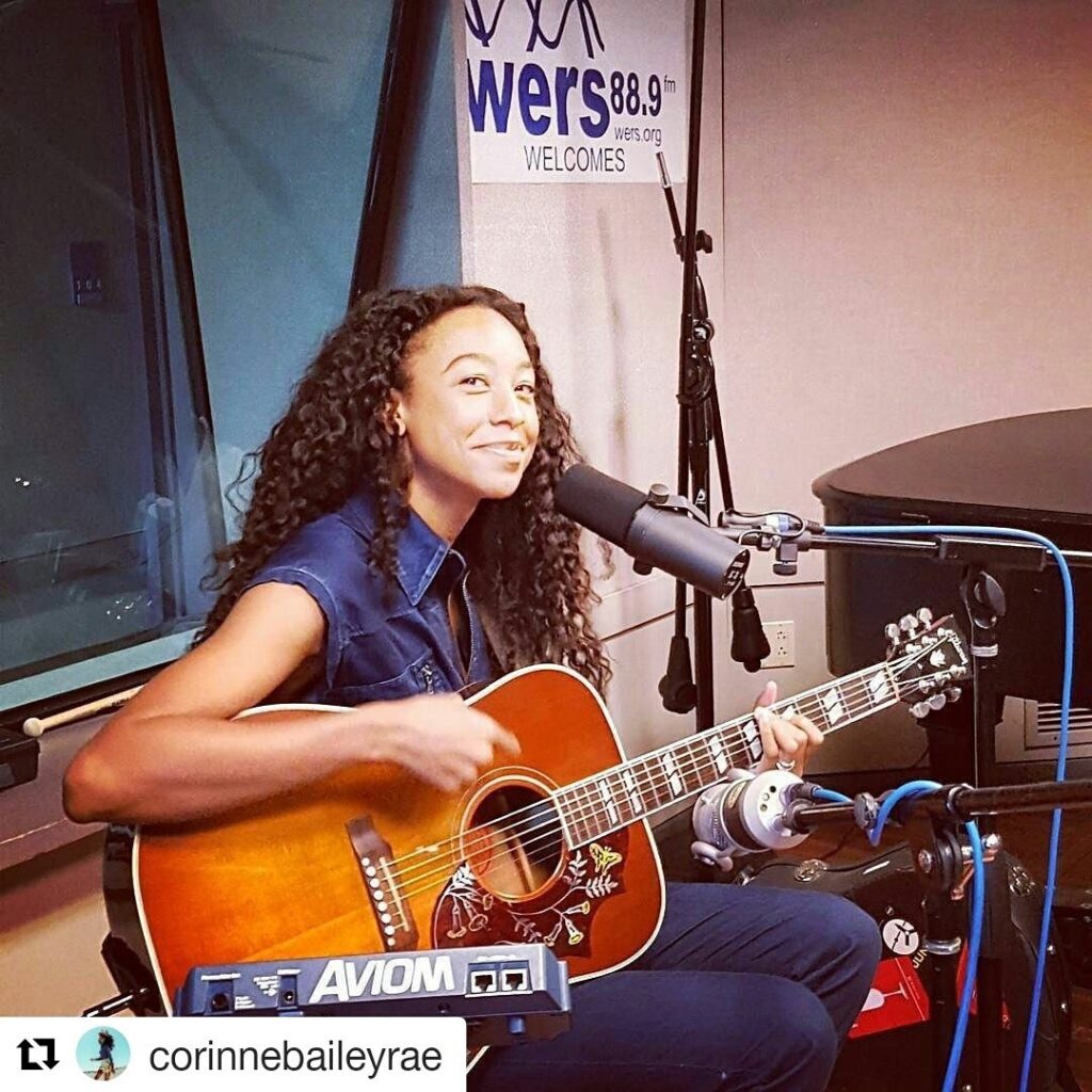 Corinne Bailey Rae sits smiling while holding a guitar