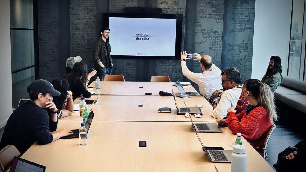 Matt Berry stands in front of a projector screen while people sit at a table in front of him