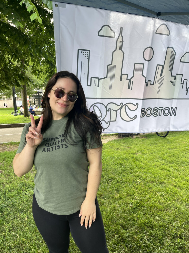 Hannah McEachern stands in front of a QTCboston poster