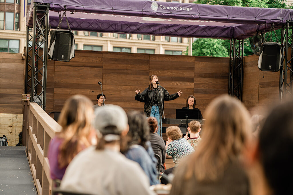 Woman sings on outdoor stage as audience watches