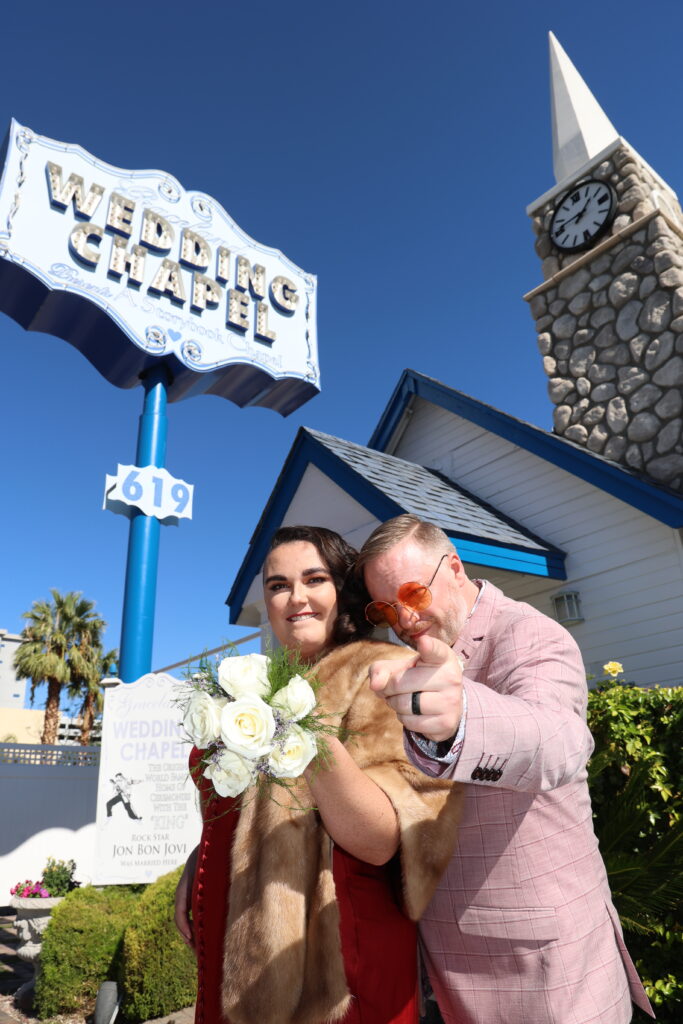 Rhiannon Jenkins and Christopher Griswold-Jenkins point at the camera outside a wedding chapel