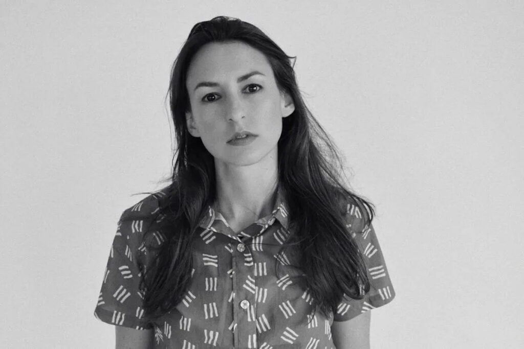 Black and white image of white woman with long dark hair, wearing button-down short sleeved shirt