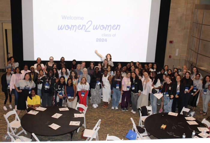 Attendees of the Women2Women Conference stand in front of large projection screen