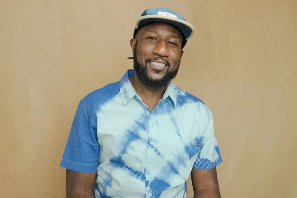 Black man wearing blue and white tie-dyed collared shirt and flat brimmed cap