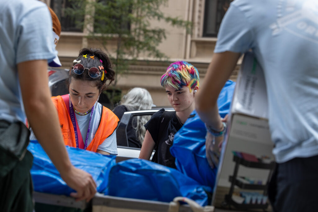 a student with multi colored hair watches as their stuff is placed in a cart