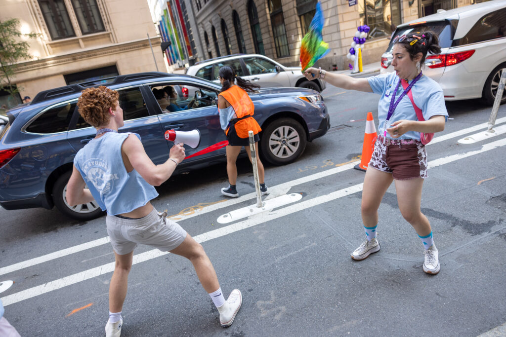 Two students sing/dance at each other while another talks to people in a vehicle