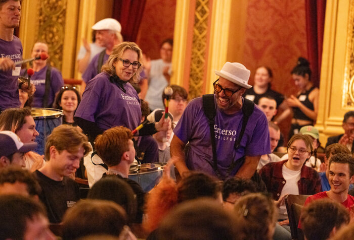 People wearing purple Emerson T-shirts play drums inside theater as audience smiles and claps