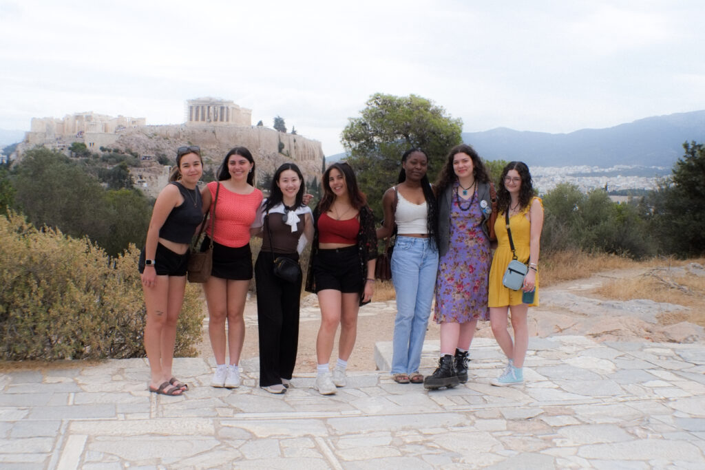 Seven students stand with the Parthenon behind them