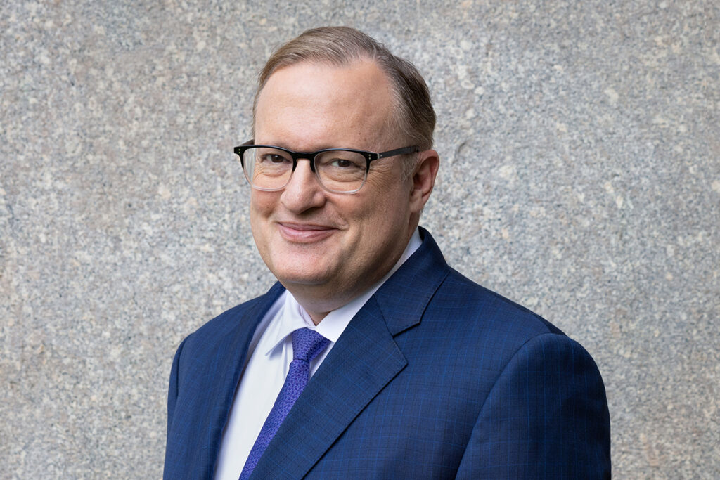 man in glasses, blue suit, in front of granite wall