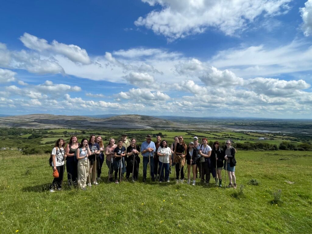 Students stand in the middle of grassy field with a blue sky and white clouds