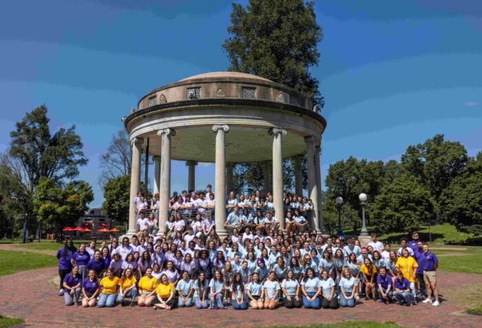 A large groupe of people pose outdoors in front of a circular structure.