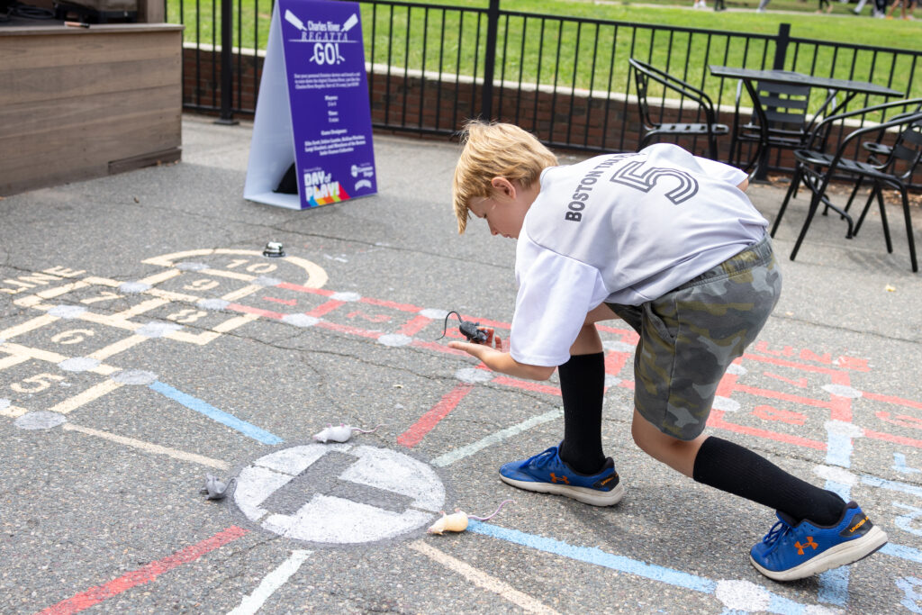 A boy leans on the hopscotch game picking up a pretend rat