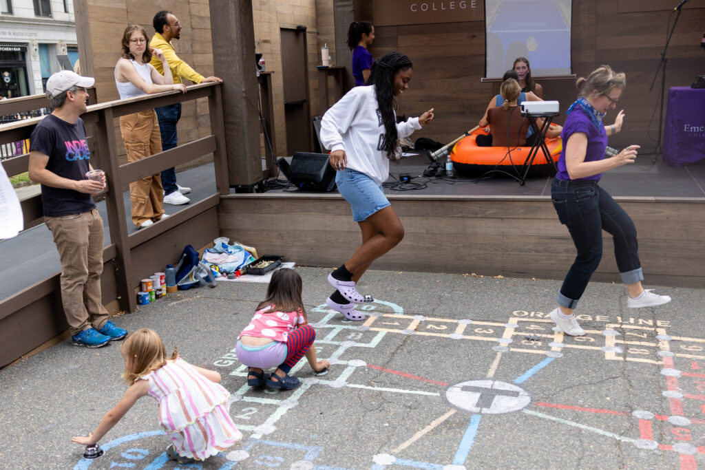 Two people hop during Difficult Hopscotch while two children kneel on the game