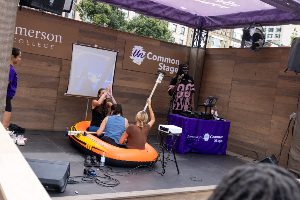 Two people sit with guitar like pieces in front of a game screen