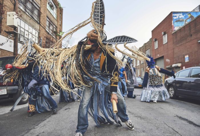 People perform in the streets, wearing colorful outfits.