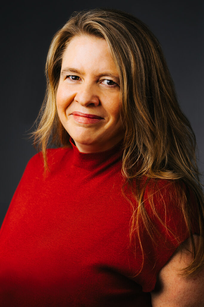 woman with long dark blonde hair, wearing red sleeveless knit top