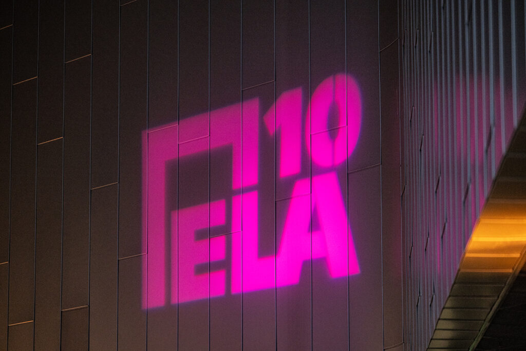 ELA 10 is projected in hot pink onto metallic side of building