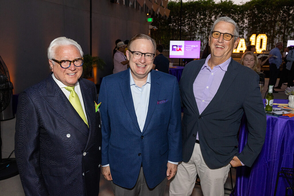 Three men in suits, black framed glasses smile for camera