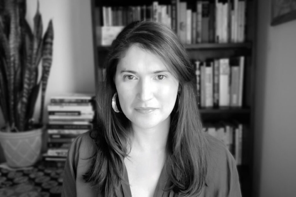 black and white photo of woman with long straight hair, wearing v-neck top, hoop earrings