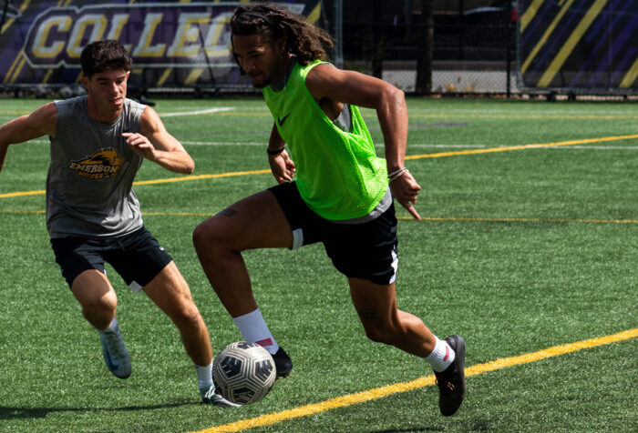 A men's soccer player dribbles away from his teammate during a practice