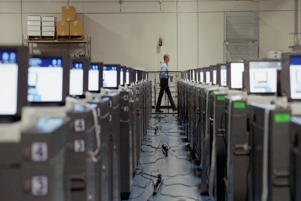 A line of voting machines with a man in the background