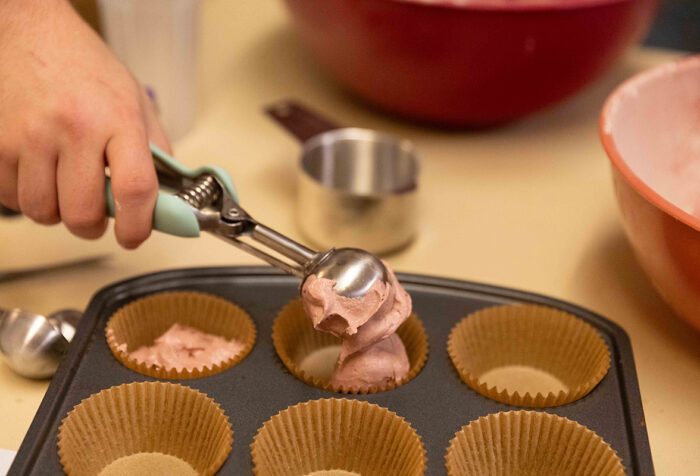 A scooper drops red velvet cupcake batter into a cupcake tin