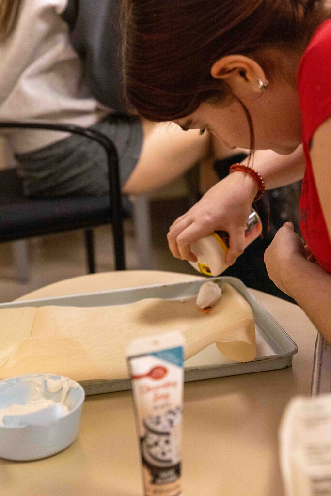 Student applies sprinkles to a white chocolate covered strawberry on a baking sheet