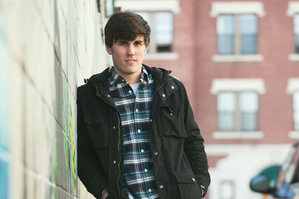 Man in plaid shirt, jacket leaning against wall