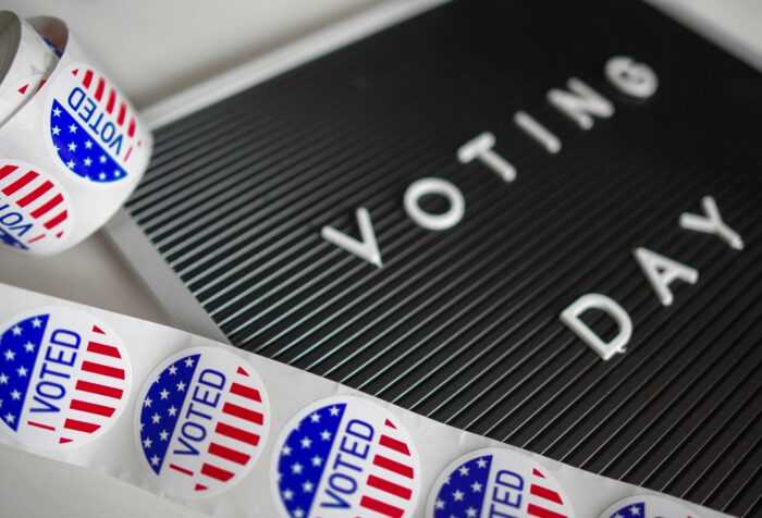 A ribbon of blue and red stickers with the words "I voted" lies next to a sign with the words "voting day."