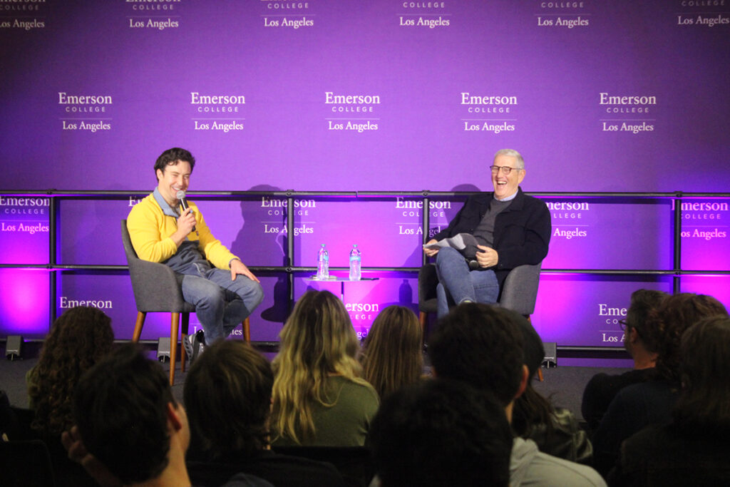 Brian Jordan Alvarez speaks into a mic while seated on stage with Doug Herzog, who is laughing