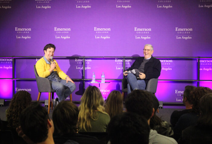 Brian Jordan Alvarez speaks into a mic while seated on stage with Doug Herzog, who is laughing