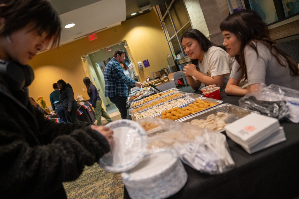 Students sit at a table of food while other students take the food