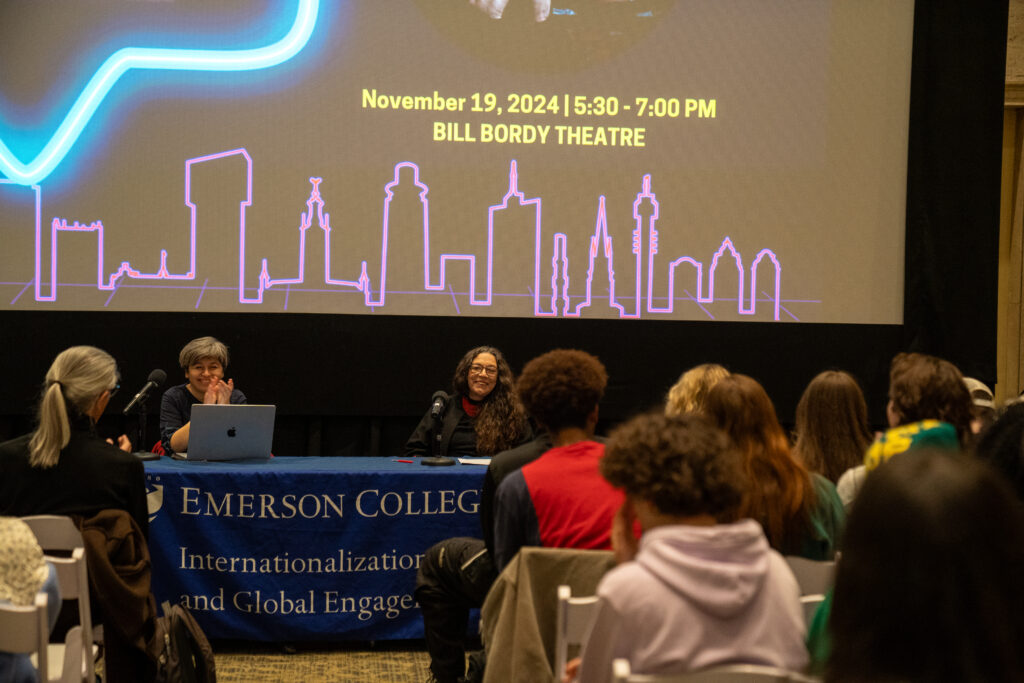 Students sit on chairs while listening to two speakers at a table in front of them