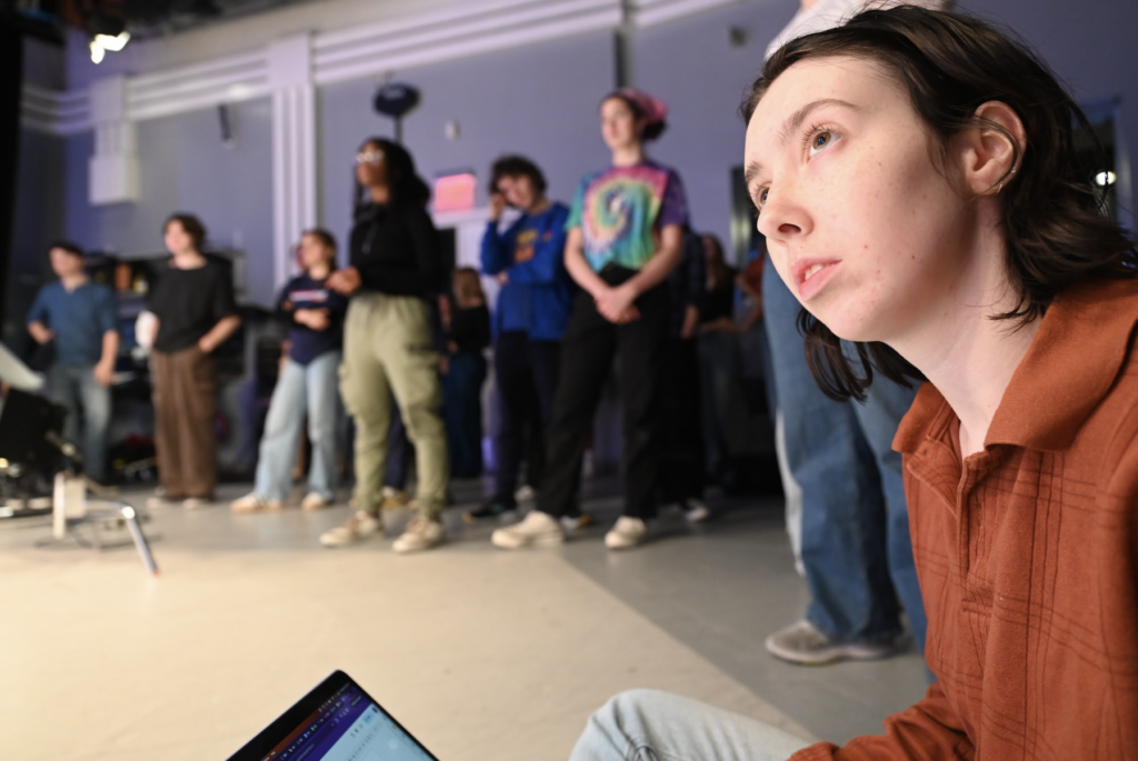 Paige Shepherd looks on with numerous production team members in background