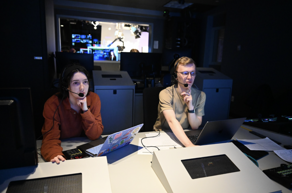 Paige Shepherd and Aidan Vahey work together with headsets on while sitting at production room desk