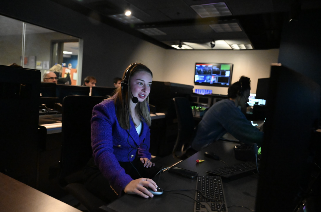 Callie Krosin works from production room computer with a headset on