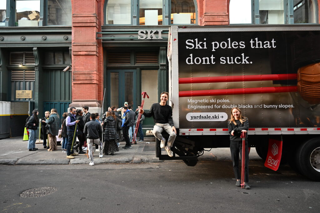 Cristina Ashbaugh and Kelly McGee by a truck that says, 'Ski poles that don't suck'