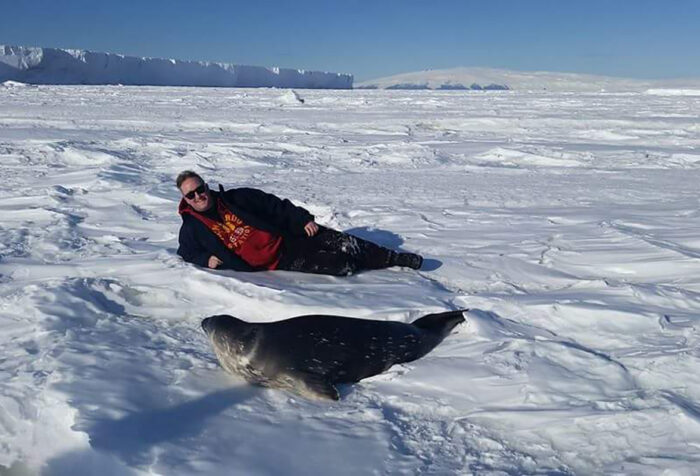 Justin Ramey lays on Antarctic ice with a seal in front of him