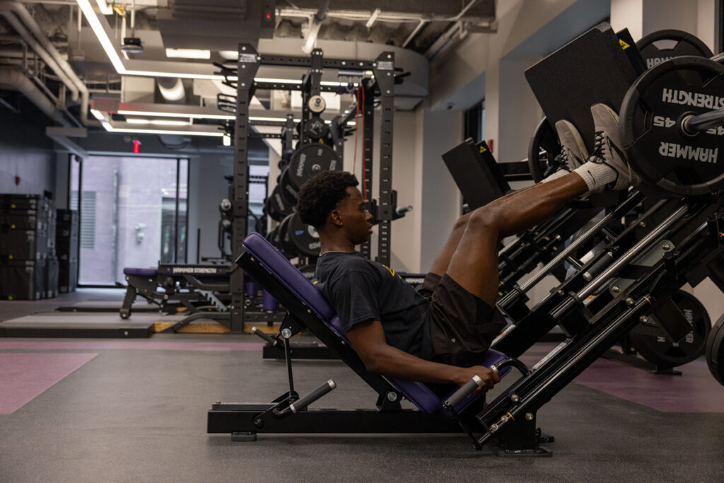 Man in black t-shirt, shorts, uses leg press