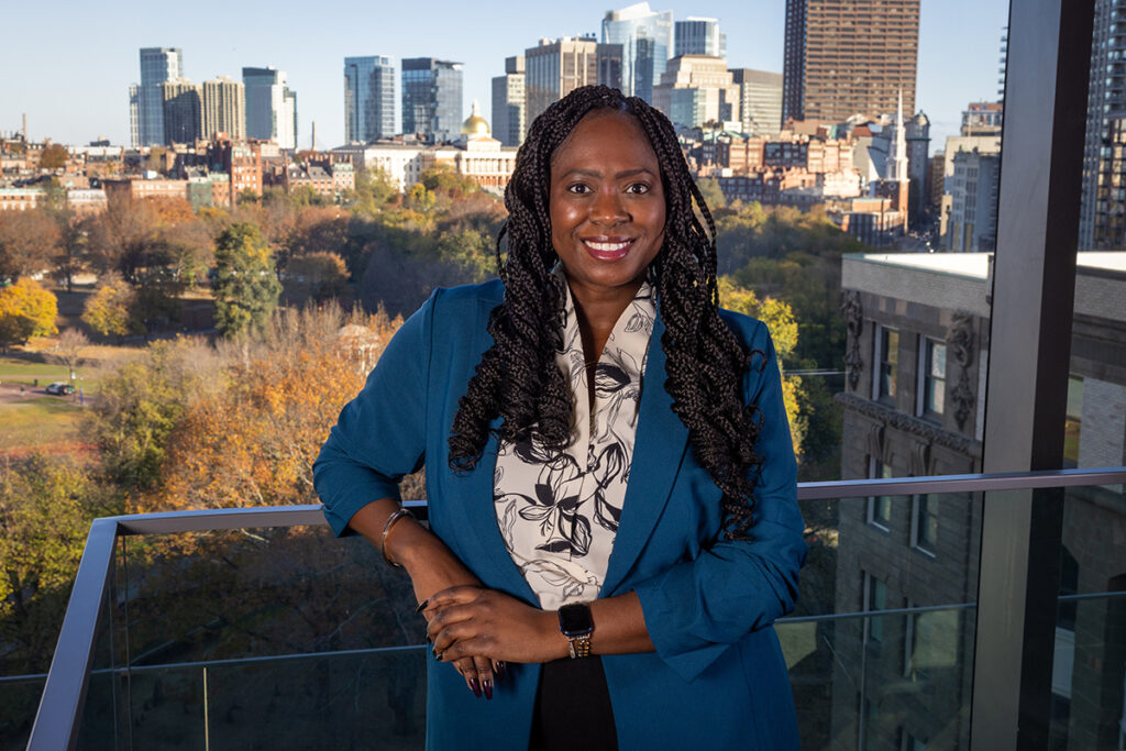 Christie Anglade in blue jacket on balcony of building overlooking Boston Common, Boston skyline