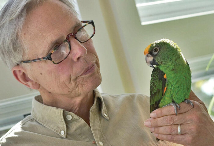 man in brown shirt, glasses, holds green parrot