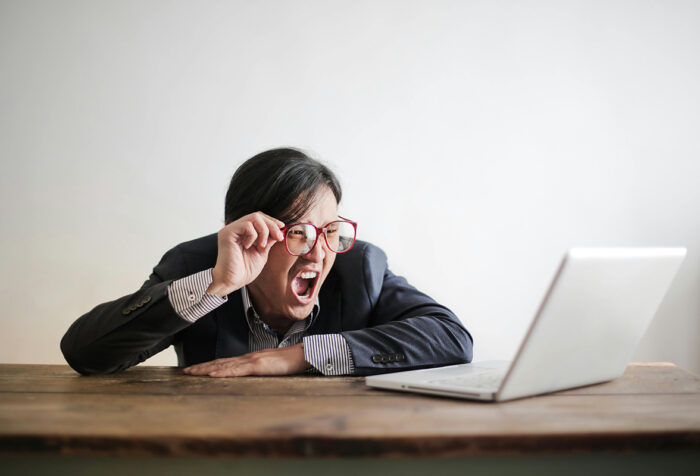 A person lifts his glasses while laughing at a laptop