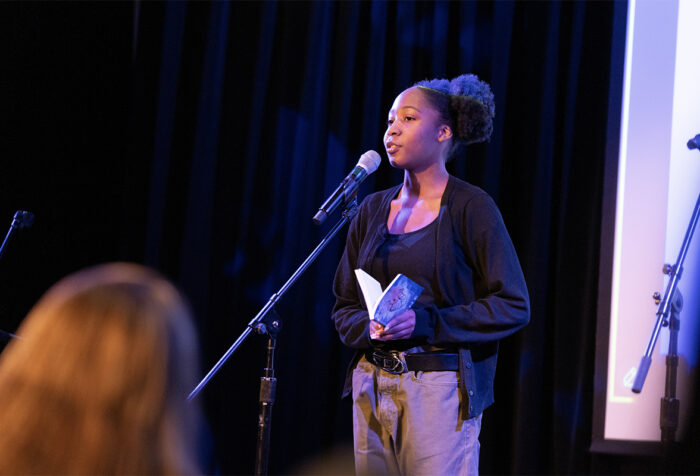 A person reads their work to the audience in front of a microphone