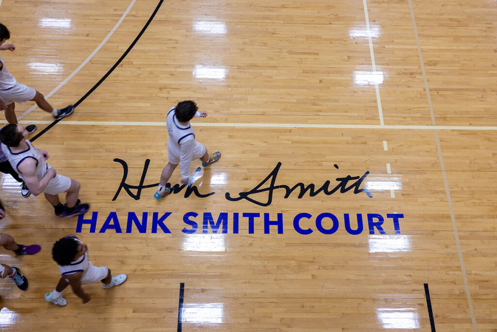 basketball players walk across a court that reads Hank Smith Court